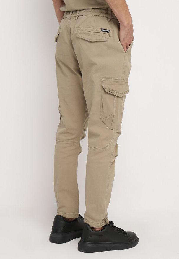 Born2be - Ciemnobeżowe Spodnie Cargo z Bawełny z Kieszeniami z Klapami Ściągane Sznurkiem Zailine. Okazja: na co dzień. Kolor: beżowy. Materiał: bawełna. Styl: klasyczny, casual, sportowy