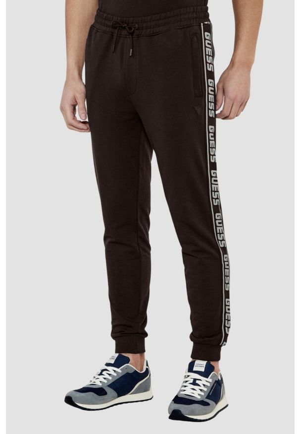 Guess - GUESS Brązowe męskie spodnie dresowe z lampasami New Arlo. Kolor: brązowy. Materiał: dresówka
