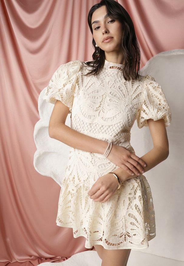 Renee - Jasnobeżowa Sukienka Amathinna. Typ kołnierza: kołnierzyk stójkowy. Kolor: beżowy. Materiał: tkanina, koronka. Wzór: jednolity, ażurowy, aplikacja, koronka. Sezon: lato. Styl: retro, wizytowy. Długość: mini