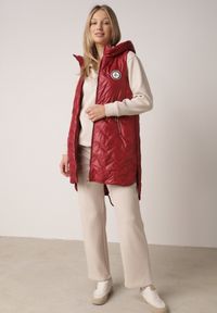 Born2be - Czerwona Przejściowa Kamizelka Pikowana o Długim Kroju z Kapturem i Naszywką Harmaste. Okazja: na co dzień. Typ kołnierza: kaptur. Kolor: czerwony. Materiał: jeans. Długość: długie. Wzór: aplikacja. Styl: casual #7