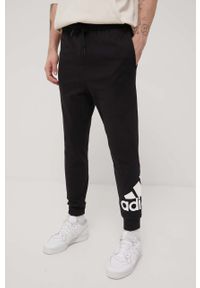 Adidas - adidas spodnie męskie kolor czarny z nadrukiem. Kolor: czarny. Materiał: poliester, materiał, bawełna. Wzór: nadruk