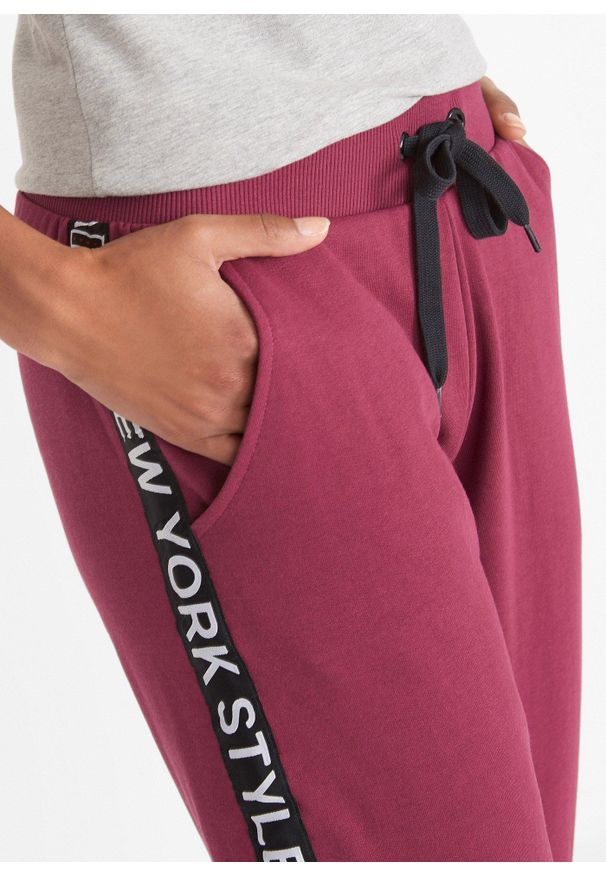 bonprix - Spodnie dresowe ze ściągaczem w talii i u dołu nogawek z napisem. Kolor: czerwony. Materiał: dresówka. Wzór: napisy