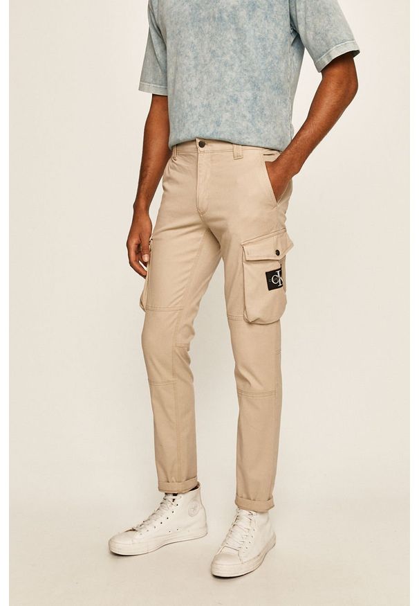 Calvin Klein Jeans - Spodnie. Kolor: beżowy. Materiał: tkanina, bawełna, elastan. Wzór: gładki
