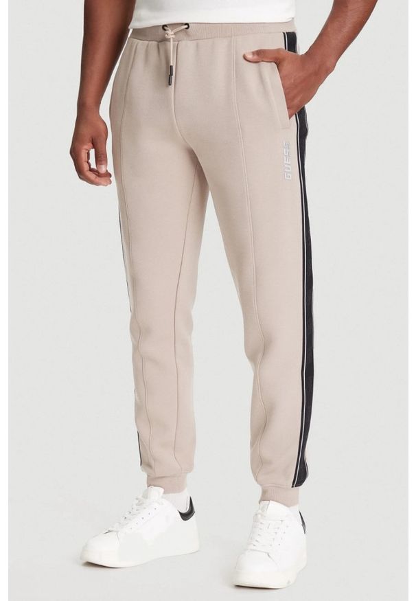 Guess - GUESS Beżowe spodnie męskie z lampasami Mickey, Rozmiar M. Kolor: beżowy