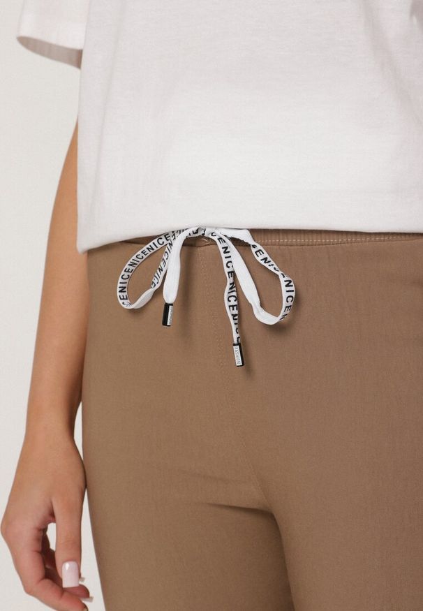 Born2be - Ciemnobeżowe Spodnie z Bawełną Ozdobione Wiązaniem Janolivra. Kolor: beżowy. Materiał: bawełna. Wzór: aplikacja