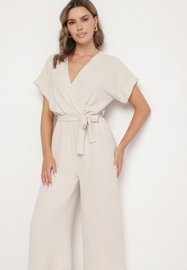 Born2be - Beżowy Kombinezon o Kopertowym Kroju z Wiązanym Paskiem Tenirea. Okazja: na co dzień. Kolor: beżowy. Długość rękawa: krótki rękaw. Długość: krótkie. Styl: casual, elegancki