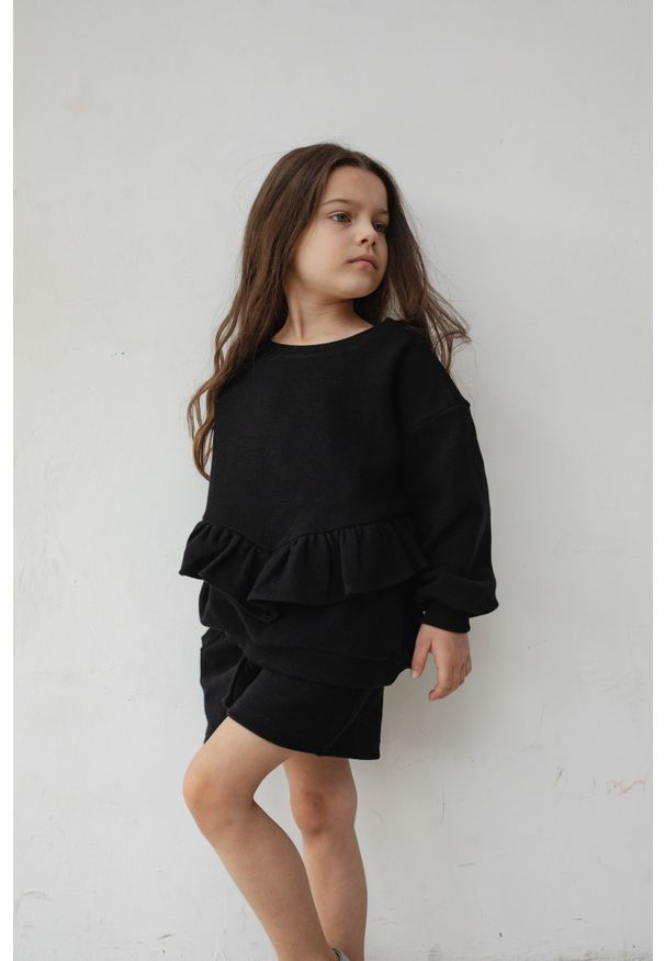 Marsala - MINI bluza oversize z falbanką z dzianiny waflowej w kolorze TOTALLY BLACK - ANGEL-80-86 (12-18). Kolor: czarny. Materiał: dzianina. Długość rękawa: długi rękaw. Długość: długie. Wzór: haft, gładki