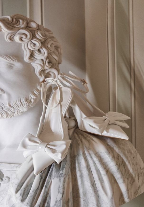 Renee - Białe Lakierowane Sandały na Szpilce Vices z Dużą Kokardką Bez Pięty Velozia. Okazja: na studniówkę, na sylwestra, na ślub cywilny, na wesele, do pracy, na spotkanie biznesowe. Zapięcie: sprzączka. Kolor: biały. Materiał: lakier. Obcas: na szpilce. Styl: wizytowy, biznesowy, elegancki