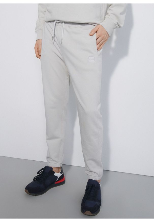 Ochnik - Kremowe spodnie dresowe męskie. Kolor: beżowy. Materiał: bawełna. Wzór: nadruk