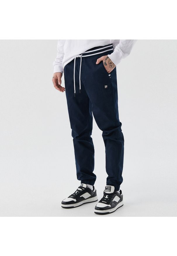 Cropp - Ciemne joggery - Granatowy. Kolor: niebieski. Materiał: bawełna, tkanina, włókno, guma. Długość: długie. Wzór: aplikacja