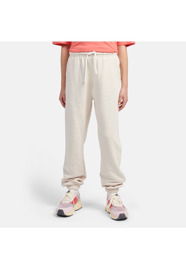 Spodnie dziecięce New Balance LAKG0058LIN – beżowe. Kolor: beżowy. Materiał: bawełna, poliester, dresówka