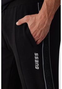 Guess - GUESS Czarne męskie spodnie dresowe z lampasami Mickey. Kolor: czarny. Materiał: dresówka