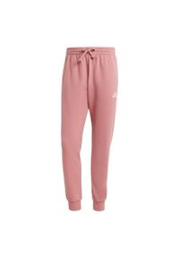 Adidas - Essentials Fleece Regular Tapered Pants. Kolor: czerwony, wielokolorowy, różowy, czarny. Materiał: materiał