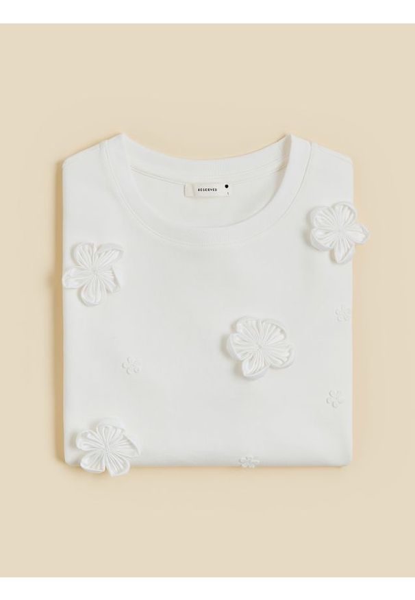 Reserved - T-shirt z kwiatową aplikacją - złamana biel. Materiał: dzianina, bawełna. Wzór: kwiaty, aplikacja