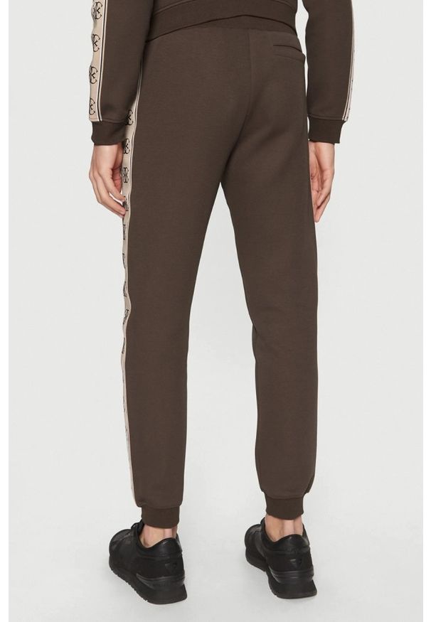 Guess - GUESS Brązowe męskie spodnie dresowe z lampasami Mickey, Rozmiar S. Kolor: brązowy. Materiał: dresówka