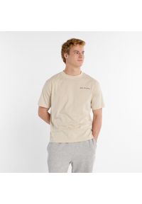 Koszulka męska New Balance MT51507TWF – beżowa. Kolor: beżowy. Materiał: dresówka, bawełna. Wzór: napisy, aplikacja