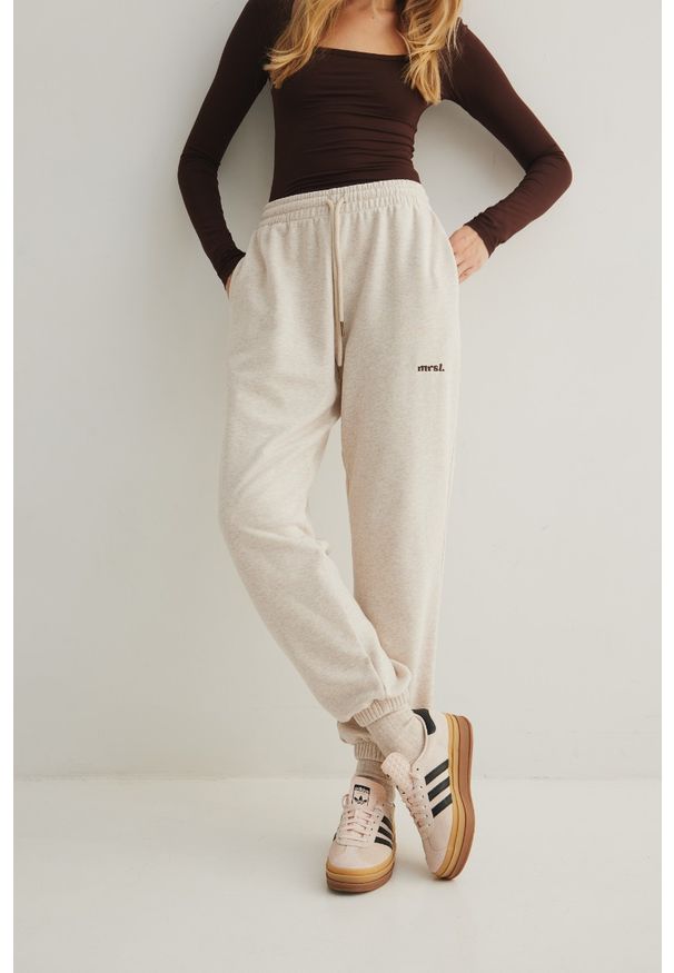 Marsala - Spodnie typu jogger w kolorze LATTE MELANGE - AUSTIN. Stan: podwyższony. Materiał: dzianina, bawełna, poliester, dresówka. Wzór: haft, melanż, aplikacja. Styl: elegancki