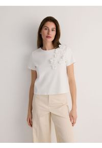 Reserved - T-shirt z kwiatową aplikacją - złamana biel. Materiał: dzianina, bawełna. Wzór: kwiaty, aplikacja