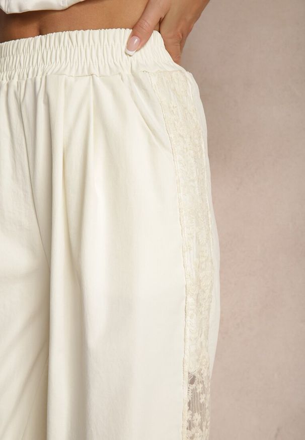Renee - Jasnobeżowe Szerokie Spodnie z Bawełną High Waist Ozdobione Koronką Efandiela. Okazja: na co dzień, na imprezę. Stan: podwyższony. Kolor: beżowy. Materiał: koronka, bawełna. Długość: długie. Wzór: koronka, aplikacja. Styl: casual, elegancki