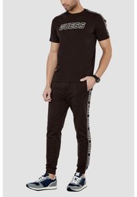 Guess - GUESS Brązowe męskie spodnie dresowe z lampasami New Arlo, Rozmiar XXL. Kolor: brązowy. Materiał: dresówka