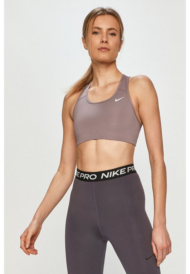 Nike - Biustonosz sportowy. Kolor: fioletowy. Materiał: włókno, skóra, tkanina. Rodzaj stanika: odpinane ramiączka. Technologia: Dri-Fit (Nike)