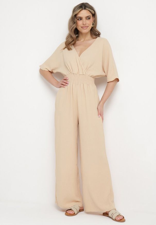 Born2be - Beżowy Taliowany Kombinezon z Kopertową Górą i Długimi Szerokimi Nogawkami Loni. Okazja: na co dzień. Kolor: beżowy. Długość: długie. Styl: klasyczny, casual, elegancki
