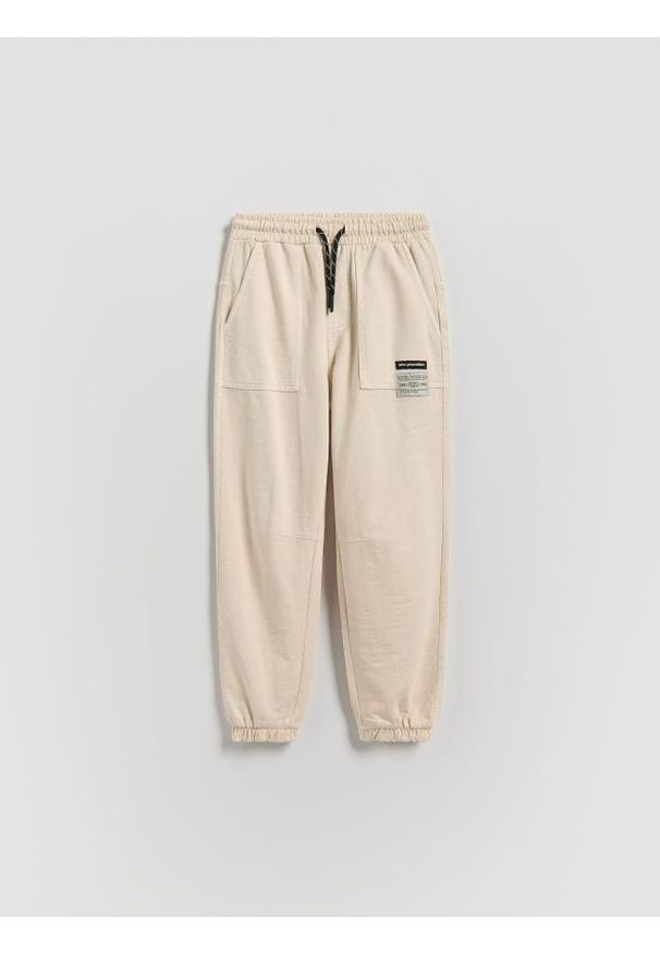 Reserved - Joggery z efektem sprania - kremowy. Kolor: kremowy. Materiał: dzianina, bawełna