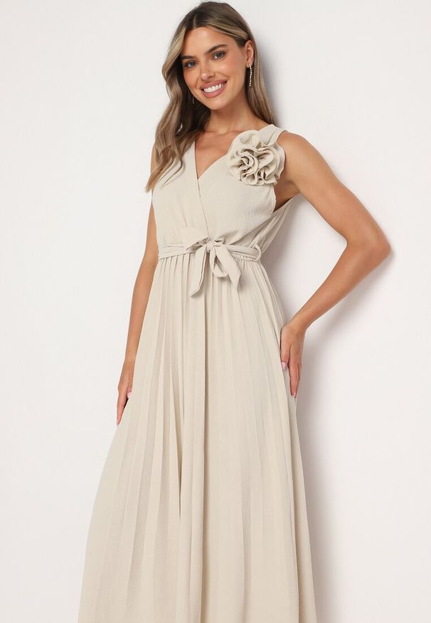 Born2be - Beżowa Plisowana Sukienka z Paskiem i Gumką w Talii Ozdobiona Broszką Kwiatem Vikmirra. Okazja: na randkę, na wesele, na ślub cywilny, na imprezę. Typ kołnierza: dekolt w kształcie V. Kolor: beżowy. Wzór: aplikacja, kwiaty. Styl: elegancki, klasyczny