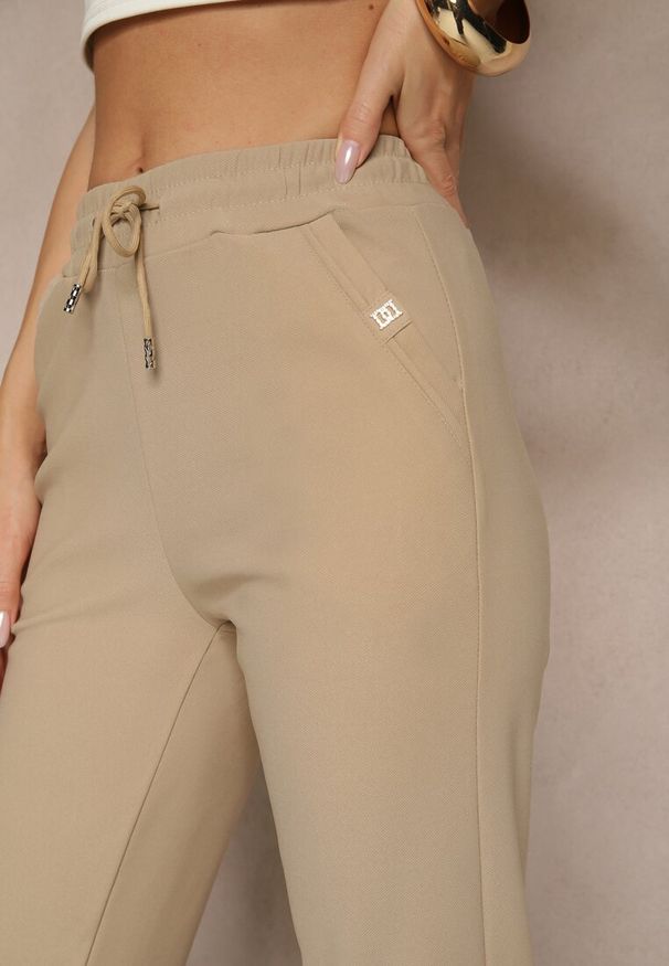 Renee - Jasnobeżowe Spodnie o Szerokim Kroju z Metalicznymi Ozdobami i Wiązaniem Voressa. Okazja: na co dzień. Kolor: beżowy. Wzór: aplikacja. Styl: casual, klasyczny