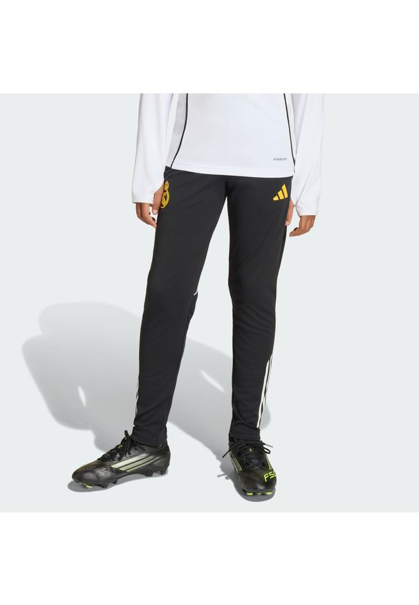 Adidas - Dziecięce spodnie treningowe adidas Real Madrid Avengers 25/26 Tiro25. Kolor: żółty, czarny, wielokolorowy, biały. Materiał: dresówka. Wzór: motyw z bajki. Sport: piłka nożna