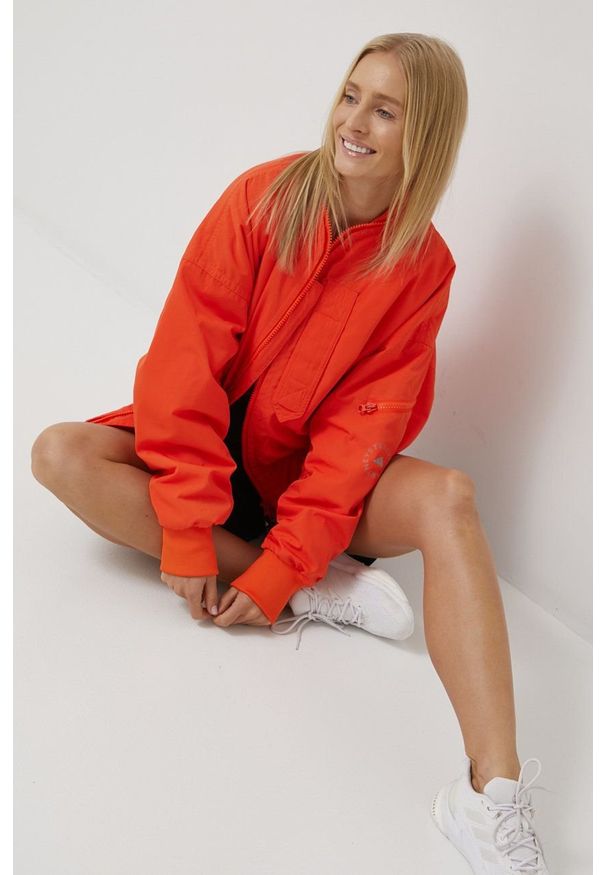Adidas by Stella McCartney - adidas by Stella McCartney wiatrówka H59970 kolor pomarańczowy przejściowa oversize. Typ kołnierza: kołnierzyk stójkowy. Kolor: pomarańczowy. Materiał: tkanina, materiał. Wzór: ze splotem